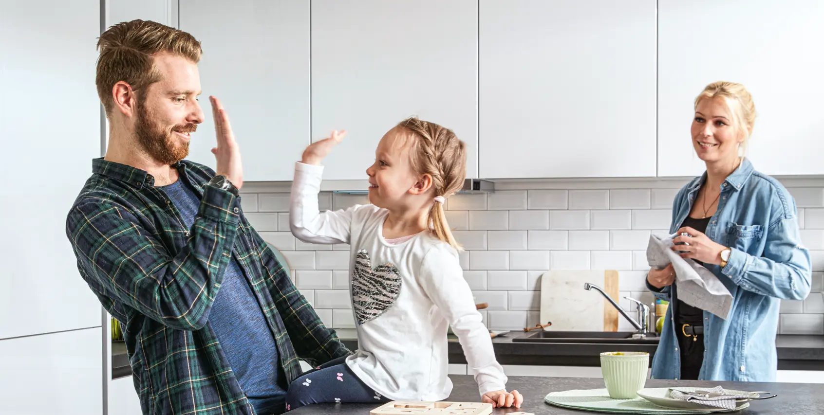 Junge Familie in moderner weißer Küche mit Eltern und Kind beim gemeinsamen Spielen und Kochen, hochwertige Einbauküche mit klaren Fronten, Wohnküche als Mittelpunkt für Alltag, Familie und gemeinsames Leben.